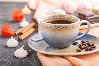 A cup of coffee with chocolate and coconut candies on a black concrete background and orange