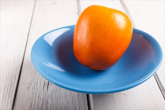 Ripe orange persimmon in a blue plate on white wooden background, with copy space