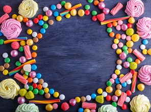 Colorful frame of multicolored candies on black wooden background. Circle copy space, top view,