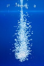 A thin jet of water penetrates the water surface and produces many air bubbles in the blue water of