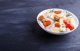 Chicken fillet salad with rosemary, pineapple and cherry tomatoes on dark blue wooden background.