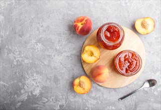 Peach jam in a glass jar with fresh fruits on gray concrete background. top view, flat lay, copy
