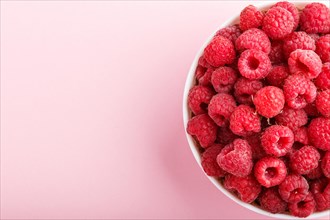 Fresh raspberry in white bowl on pink pastel background. top view, copy space, close up