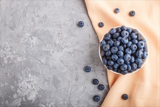 Fresh blueberry in white bowl and orange pastel textile on gray concrete background. top view, flat