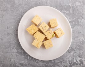 Traditional indian candy soan papdi in white plate with almond and pistache on a gray concrete