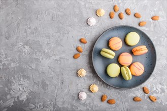 Orange and green macarons or macaroons cakes on blue ceramic plate on a gray concrete background.