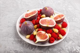 Fresh figs, strawberries and raspberries on white ceramic plate on gray concrete background. side