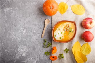 Traditional pumpkin cream soup with seeds in clay bowl on a gray concrete background with linen