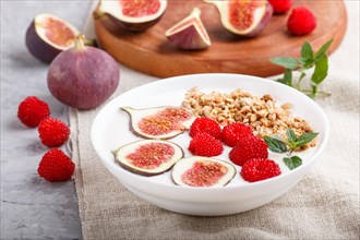 Yoghurt with raspberry, granola and figs in white plate on a gray concrete background and linen
