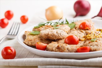 Fried pork chops with tomatoes and herbs on a white ceramic plate on a white wooden background and
