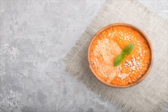 Carrot cream soup with sesame seeds in wooden bowl on a gray concrete background with linen textile
