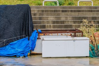Old abandoned refrigerator laying on wet concrete in front of stairway on rainy morning in South