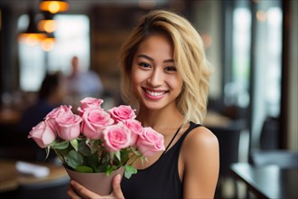 Smiling Asian woman with blond hair holding bouet of pink rose flowers on dare in restaurant. KI