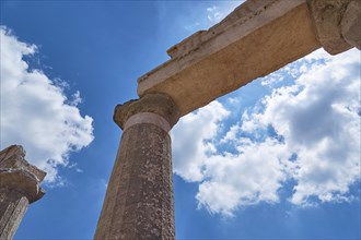 View upwards along ancient columns into the blue sky with white clouds, Archaeological site,