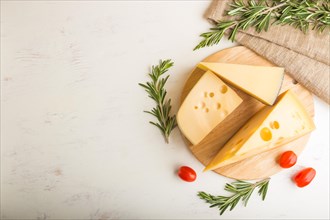 Various types of cheese with rosemary and tomatoes on wooden board on a white wooden background and