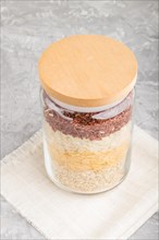 Glass jar with different kinds of rice poured in layers on a gray concrete background. side view,