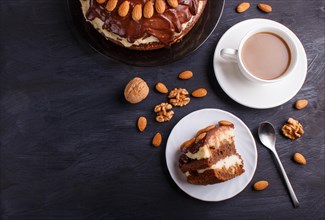 Homemade chocolate cake with milk cream, caramel and almonds on black wooden background. cup of