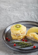 Pieces of baked pork with pineapple, cheese and kiwi on gray plate, side view, close up, selective