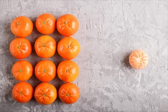 Rows of tangerines forming a rectangle and one peeled tangerine on a gray concrete background, top