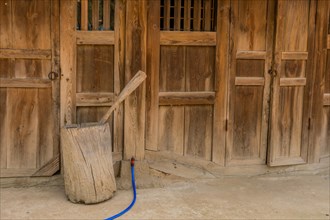 Wooden hand grain pulverizer in front of wooden building in public park displaying traditional
