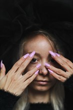 A striking image of a young blonde caucasian woman with purple nails covering her face with both