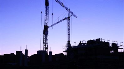 Construction site with cranes at nightfall with the silhouettes of the houses and the cranes