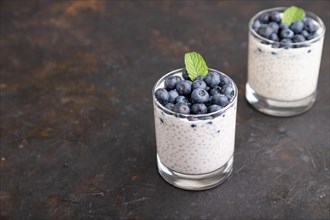 Yogurt with blueberry and chia in glass on black concrete background. Side view, close up, copy