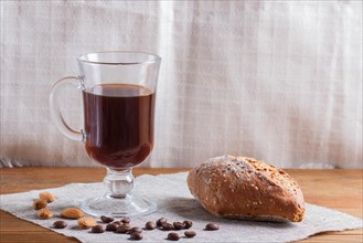 Glass cup of coffee with bun on a wooden background and linen textile. close up, copy space