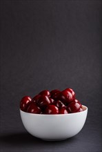 Fresh red sweet cherry in white bowl on black background. side view, copy space