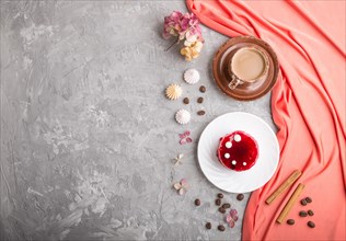 Red cake with souffle cream with cup of coffee on a gray concrete background and red textile. top