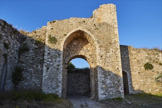 Old castle gate in a stone ruin surrounded by grass and clear blue sky above, sea fortress Methoni,