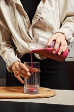 Unrecognizable woman pouring banana and black currant smoothie in glass in the kitchen