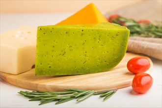 Green basil cheese and various types of cheese with rosemary and tomatoes on wooden board on a