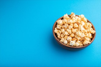 Popcorn with caramel in wooden bowl on a pastel blue background. Side view, copy space