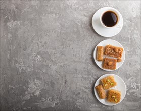 Traditional arabic sweets (basbus, kunafa, baklava) on white plate and a cup of coffee on a gray