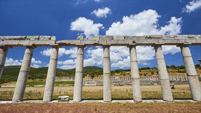 Partially reconstructed ancient row of columns in front of an ancient stadium, under a blue sky,