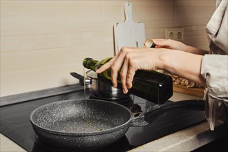Unrecognizable woman pouring olive oil on skillet from the bottle, side view