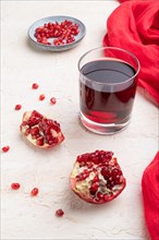 Glass of pomegranate juice on a white concrete background with red textile. Side view, close up