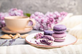 Purple macarons or macaroons cakes with cup of coffee on a gray wooden background and white linen