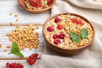 Wheat flakes porridge with milk, raspberry and currant in wooden bowl on white wooden background