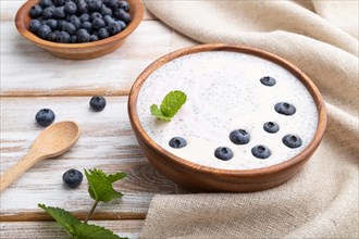 Yogurt with blueberry in wooden bowl on white wooden background and linen textile. Side view, close