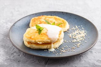 Cheese pancakes on a blue ceramic plate with milk sauce on a gray concrete background. side view,