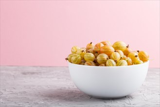 Fresh green gooseberry in white bowl on gray and pink background. side view, copy space, close up
