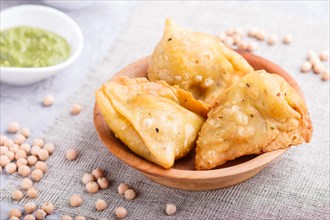 Traditional indian food samosa in wooden plate with mint chutney on a gray concrete background.