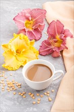 Yellow anf purple day-lilies cup of coffee on a gray concrete background, with orange textile.
