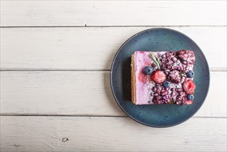 Berry cake with milk cream and blueberry jam on blue ceramic plate on a white wooden background.