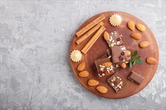A pieces of milk chocolate with almonds and dried fruits on a brown wooden board on a gray concrete