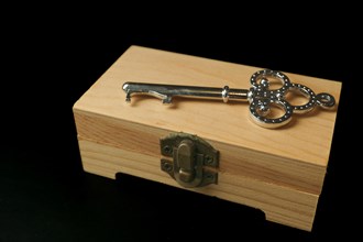 Closed wooden box with a metal key on top isolated on black background and copyspace