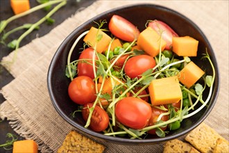 Vegetarian vegetable salad of tomatoes, pumpkin, microgreen pea sprouts on black concrete