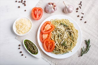 Spaghetti pasta with pesto sauce, tomatoes and cheese on a linen tablecloth on white wooden
